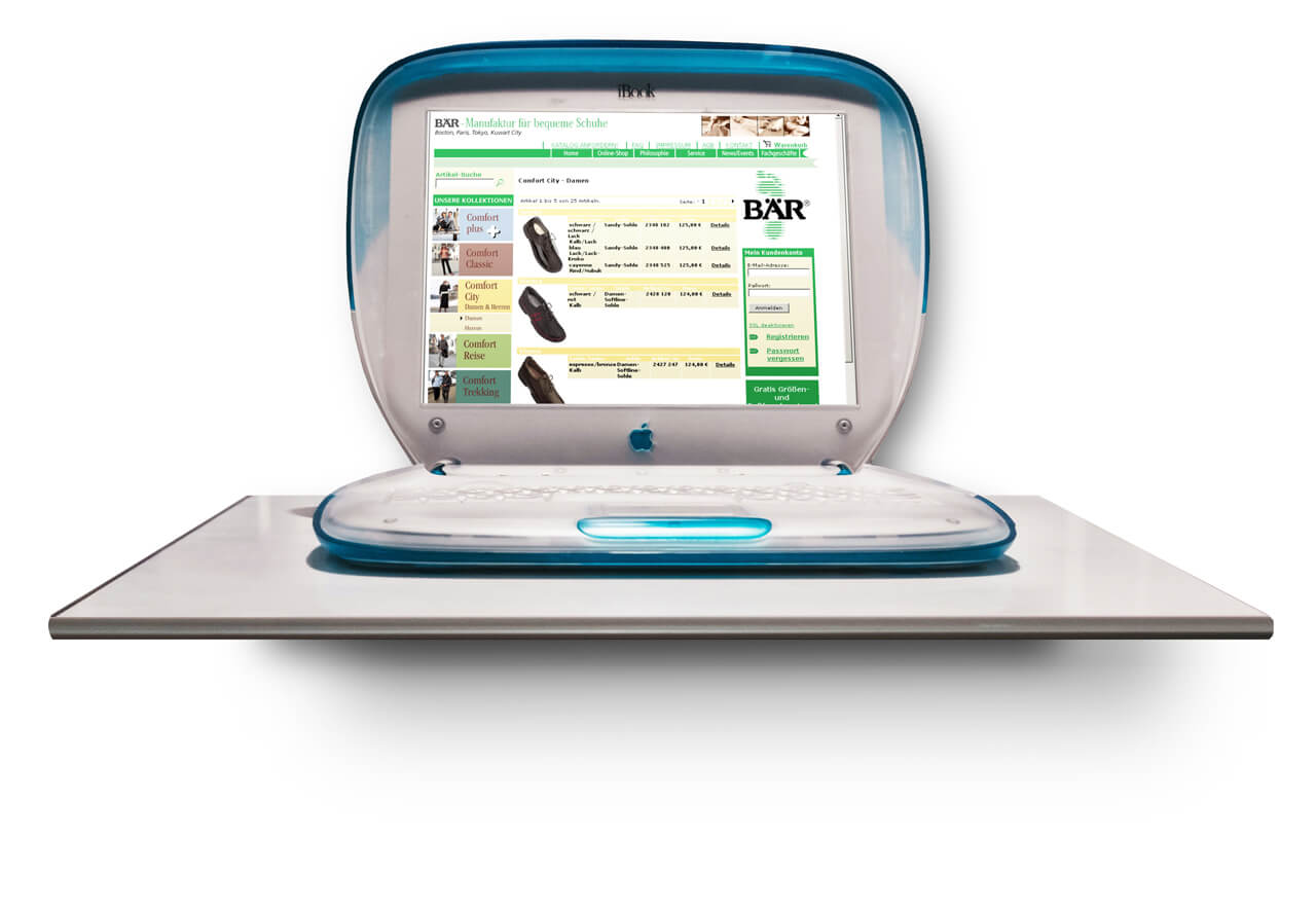 Open blue and white vintage Apple iBook laptop showing a shoe retailer's website with product listings on the screen