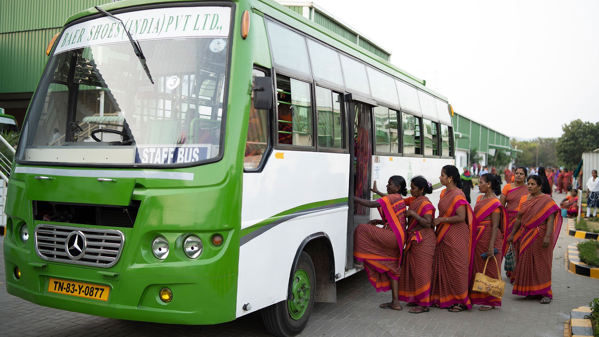 Mitarbeiterinnen steigen in grünen Firmenbus ein Gruppe von Frauen in traditionellen Saris beim Einsteigen in einen grünen Unternehmensbus vor einer Fabrik