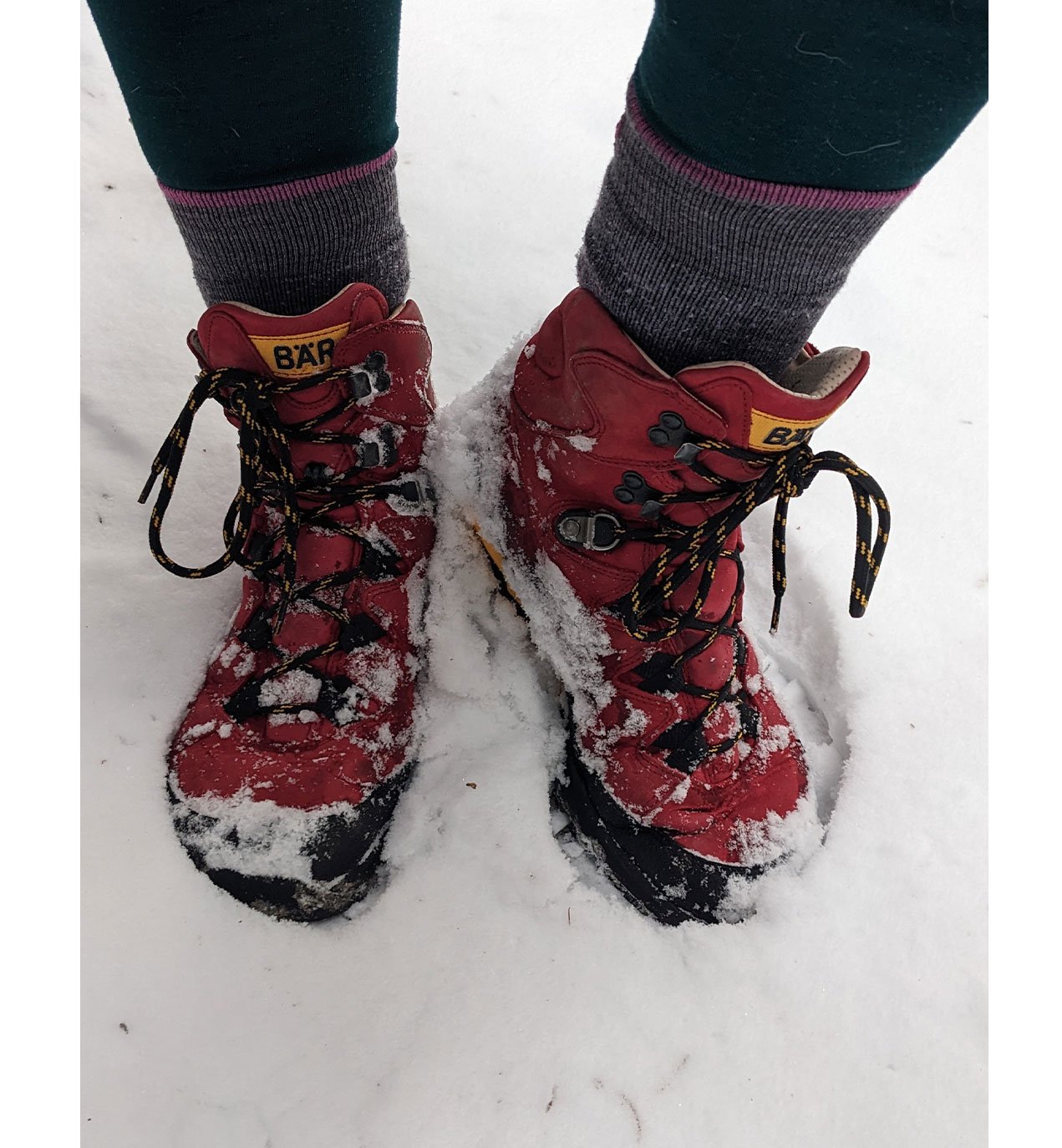 Rote Wanderschuhe im Schnee Rote Wanderschuhe mit Schnee bedeckt, getragen von einer Person mit grauen Socken auf verschneitem Boden.
