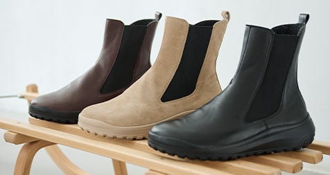 Stylish Chelsea Boots in Brown, Beige, and Black on Wooden Rack Three pairs of Chelsea boots in brown, beige, and black displayed on a wooden rack.