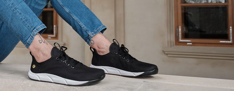 Person wearing black sneakers with white soles and blue jeans sitting on a stone ledge