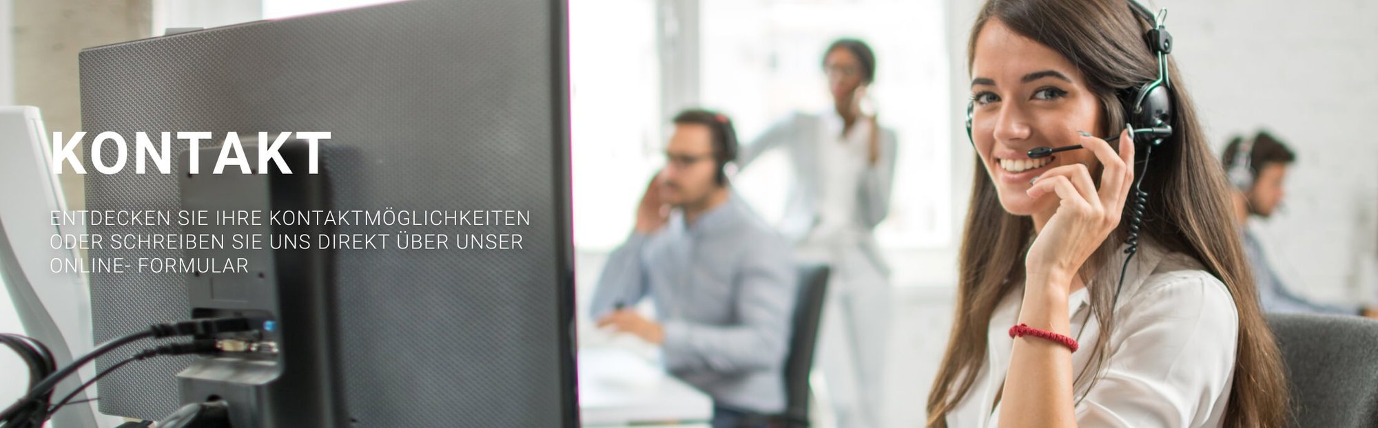 Junge Frau mit Headset lächelnd am Schreibtisch, Kollegen im Hintergrund