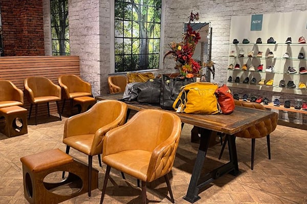 Innenansicht eines stilvoll eingerichteten Geschäfts mit Ledersesseln, Holztisch und Regalen voller Schuhe und Taschen.