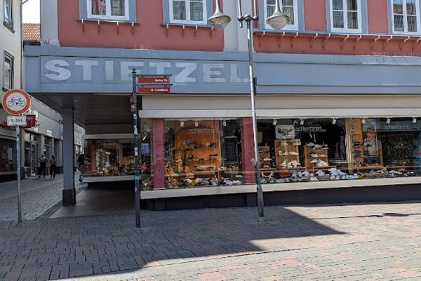 Außenansicht eines Geschäfts namens Stietzel in einer Fußgängerzone, mit Schaufenstern voller Waren und umliegenden Straßenlaternen.