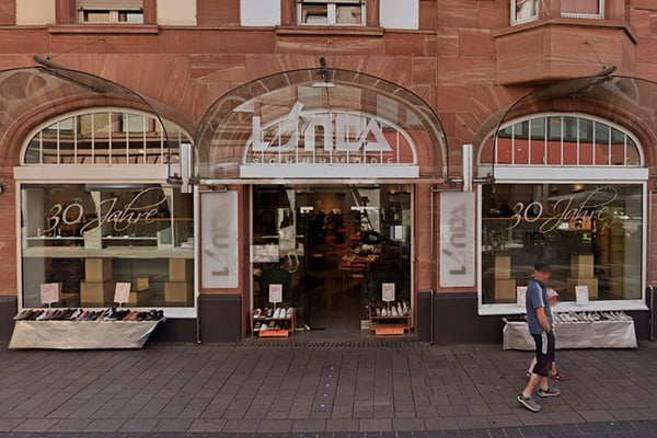 Straßenansicht eines Schuheinzelhandels mit Markise und Schaufensterauslage, zwei Personen gehen vorbei