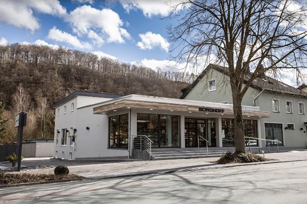 Außenansicht eines modernen Geschäftsgebäudes mit großen Fenstern, umgeben von Bäumen und einem klaren blauen Himmel.