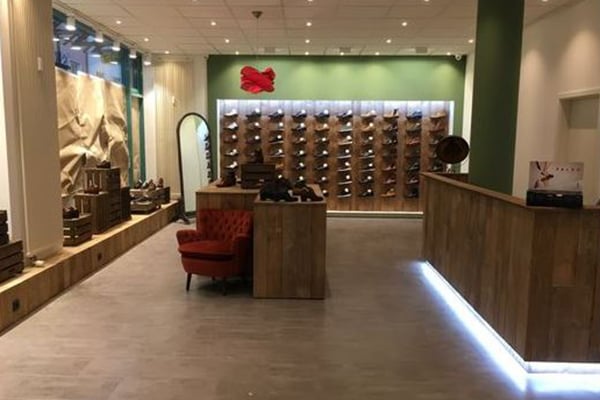 Innenansicht eines Schuhgeschäfts mit grüner Wand, elegantem Holzdekor und rotem Sessel