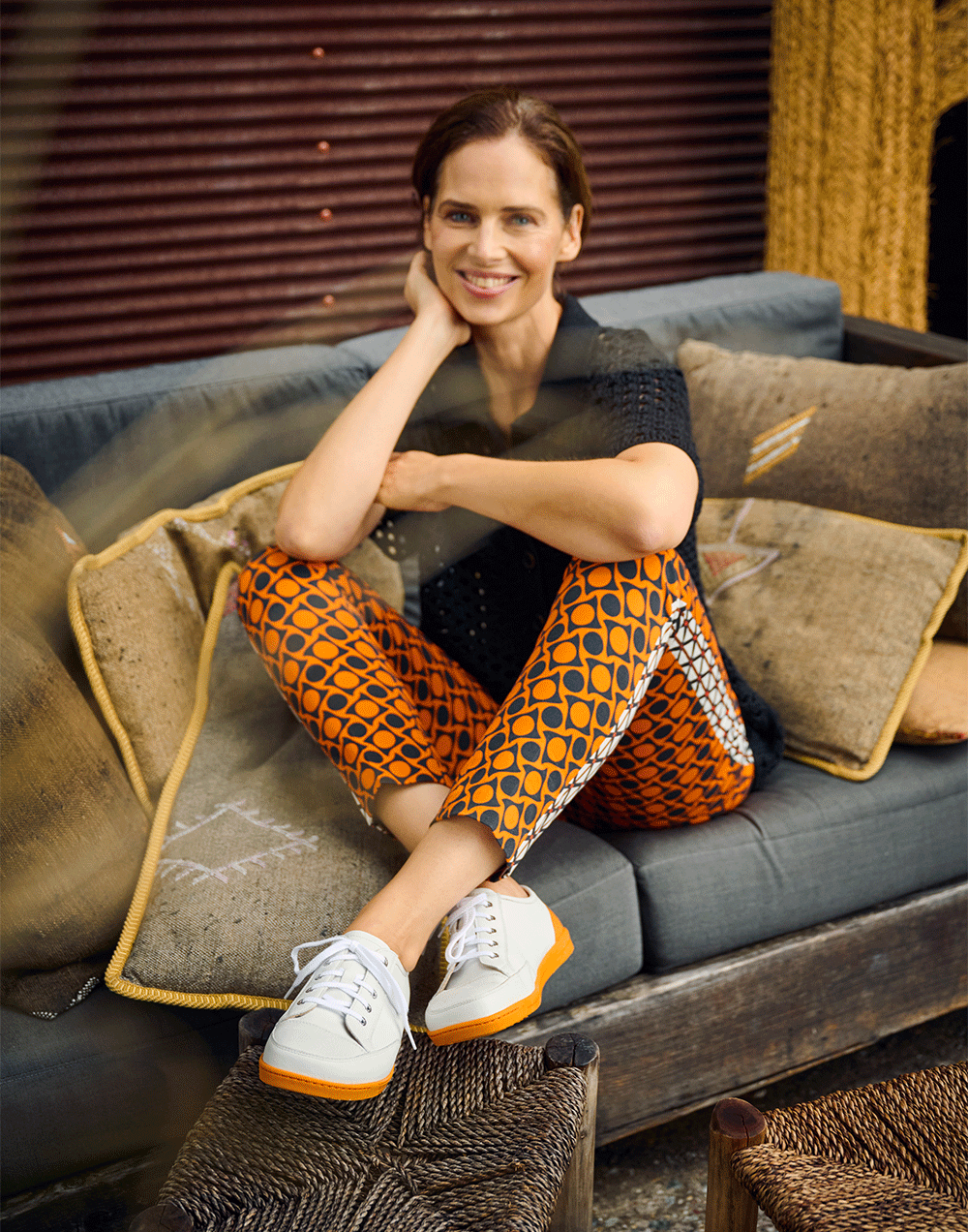 Sitzende Frau in orange-gemusterter Hose und wei&szlig;en Turnschuhen auf einem Sofa