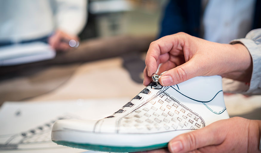 Close-up of a person adjusting a sneaker prototype with a button A close-up of hands working on a white sneaker design prototype, adjusting laces with a button in a workshop setting.