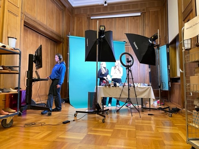 Professional photo studio setup with staff and equipment A professional photo studio featuring lighting equipment, a blue backdrop, and staff preparing for a photoshoot.