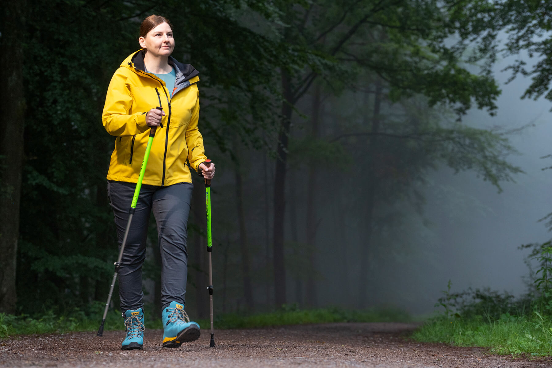 Woman hiking with poles in a misty forest in a yellow jacket A woman in a yellow jacket hiking with poles through a misty forest trail