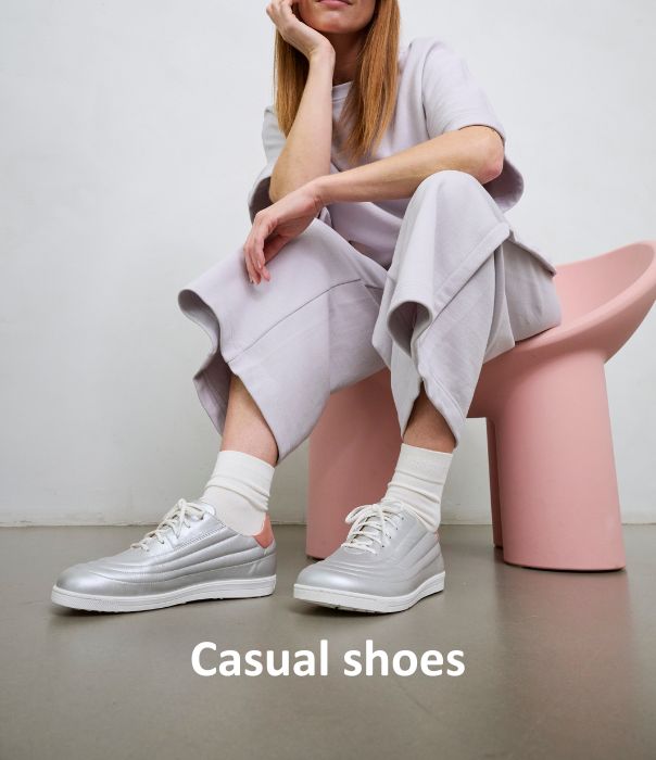 Person wearing silver casual shoes, sitting on a pink chair with crossed legs.