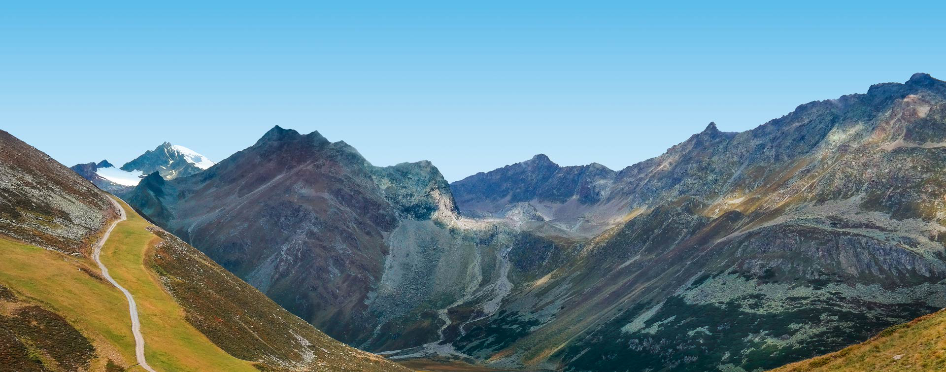 Panoramic view of a mountain range under a clear blue sky A scenic landscape of a mountain range with a winding path and a clear blue sky