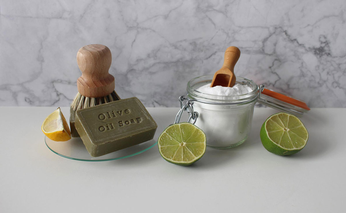 Natural cleaning essentials with olive oil soap and citrus Olive oil soap, a wooden brush, a jar of baking soda, and sliced lemons and limes for eco-friendly cleaning