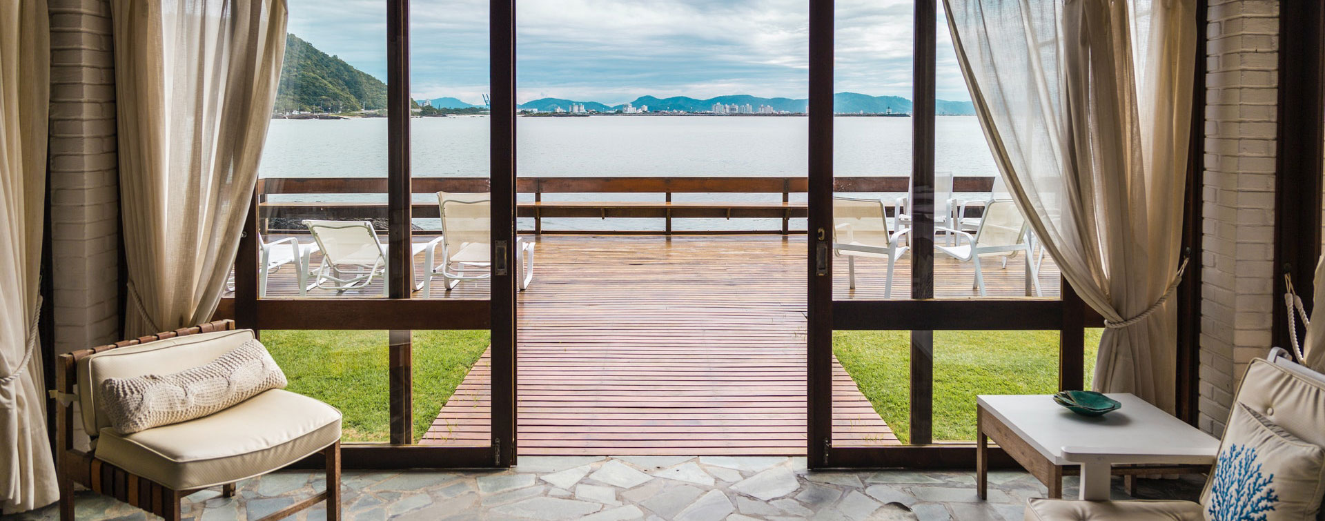 Cozy Living Room with Ocean View and Patio Living room with a view of the ocean through large glass doors, leading to a wooden patio with chairs.