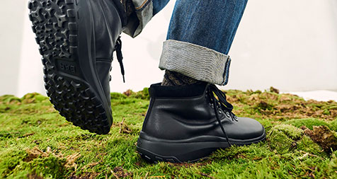 Stylish Black Ankle Boots on Mossy Ground A person wears black ankle boots with rugged soles, standing on a mossy surface, showcasing outdoor style and comfort.