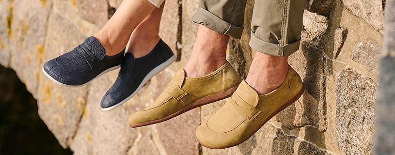 Stylish loafers for men and women walking on a stone wall Close-up of two pairs of shoes, navy slip-on sneakers for women and tan loafers for men, worn by people sitting on a stone wall