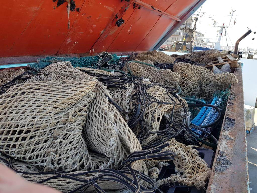 Close-up of fishing nets and ropes piled on a boat with a visible rusted metal edge and an orange canopy, docked in a harbor.