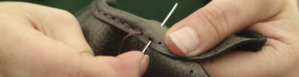 Handgefertigte Lederverarbeitung – Detailansicht Nahaufnahme einer Person, die eine Nadel verwendet, um Leder von Hand zu nähen.