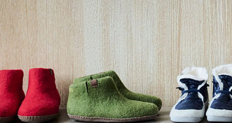 Cozy Wool Slippers in Red, Green, and Blue A row of three pairs of wool slippers in red, green, and blue colors displayed against a wooden background