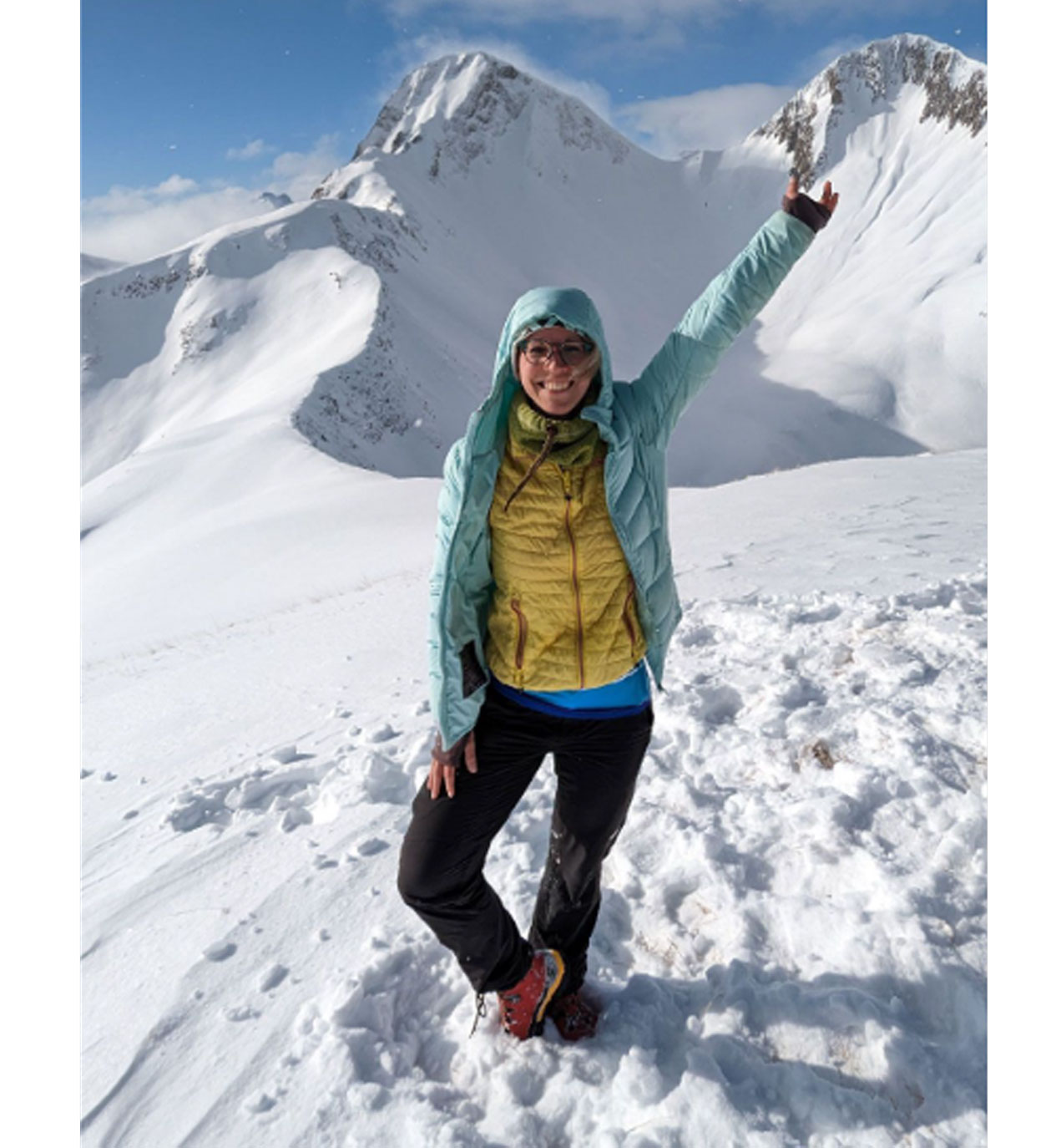 Lächelnde Frau in Winterkleidung auf Schneeberg mit erhobenem Arm