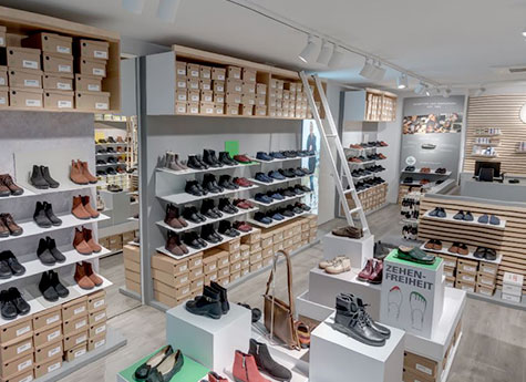 Moderner Schuhgeschäft-Innenraum mit vielfältiger Auswahl an Schuhen Innenansicht eines modernen Schuhgeschäfts mit Regalen voller Schuhe und Leitern zum Erreichen höherer Ebenen