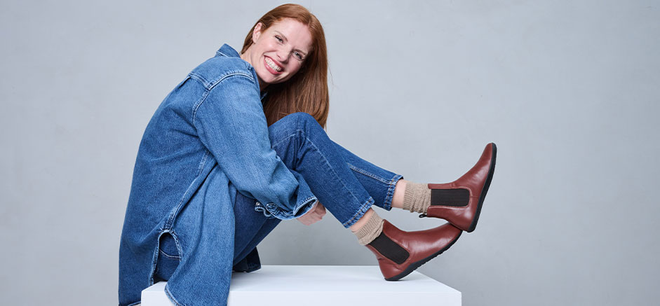 Smiling person in denim outfit and brown leather boots sitting on a white block