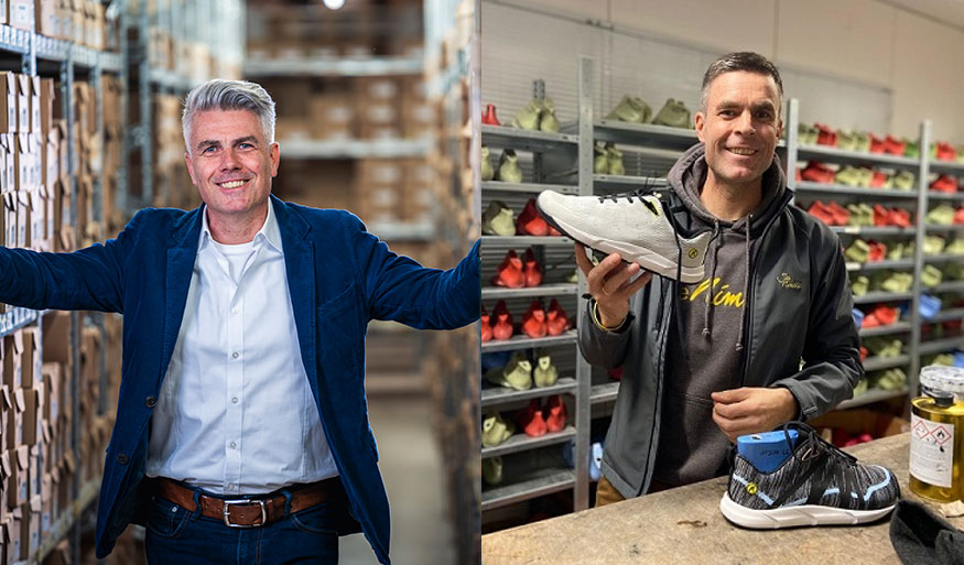 Zwei Männer in einem Lager mit Schuhen: links ein Mann in einem blauen Anzug vor Regalen mit Kartons, rechts ein Mann in dunkler Kleidung hält einen Schuh. Links ein Mann in einem Anzug in einem Lager mit Kartons, rechts ein Mann in dunkler Kleidung mit einem Schuh in der Hand, im Hintergrund Regale mit Schuhen.