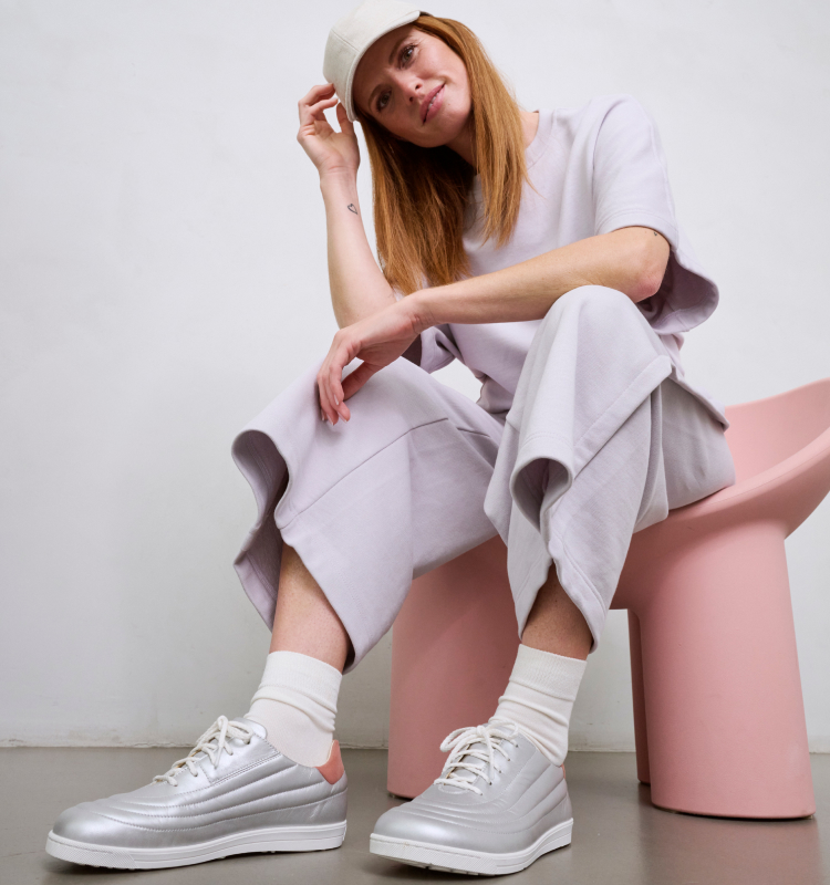 Frau in hellem Outfit und silbernen Sneakers auf rosa Stuhl sitzend