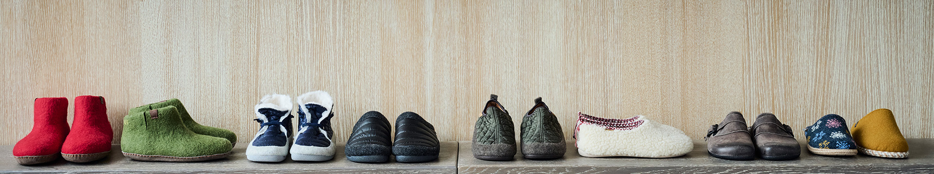 Collection of Winter Slippers in Various Colors and Designs A variety of winter slippers displayed on a wooden surface, including red, green, blue, black, and patterned designs.