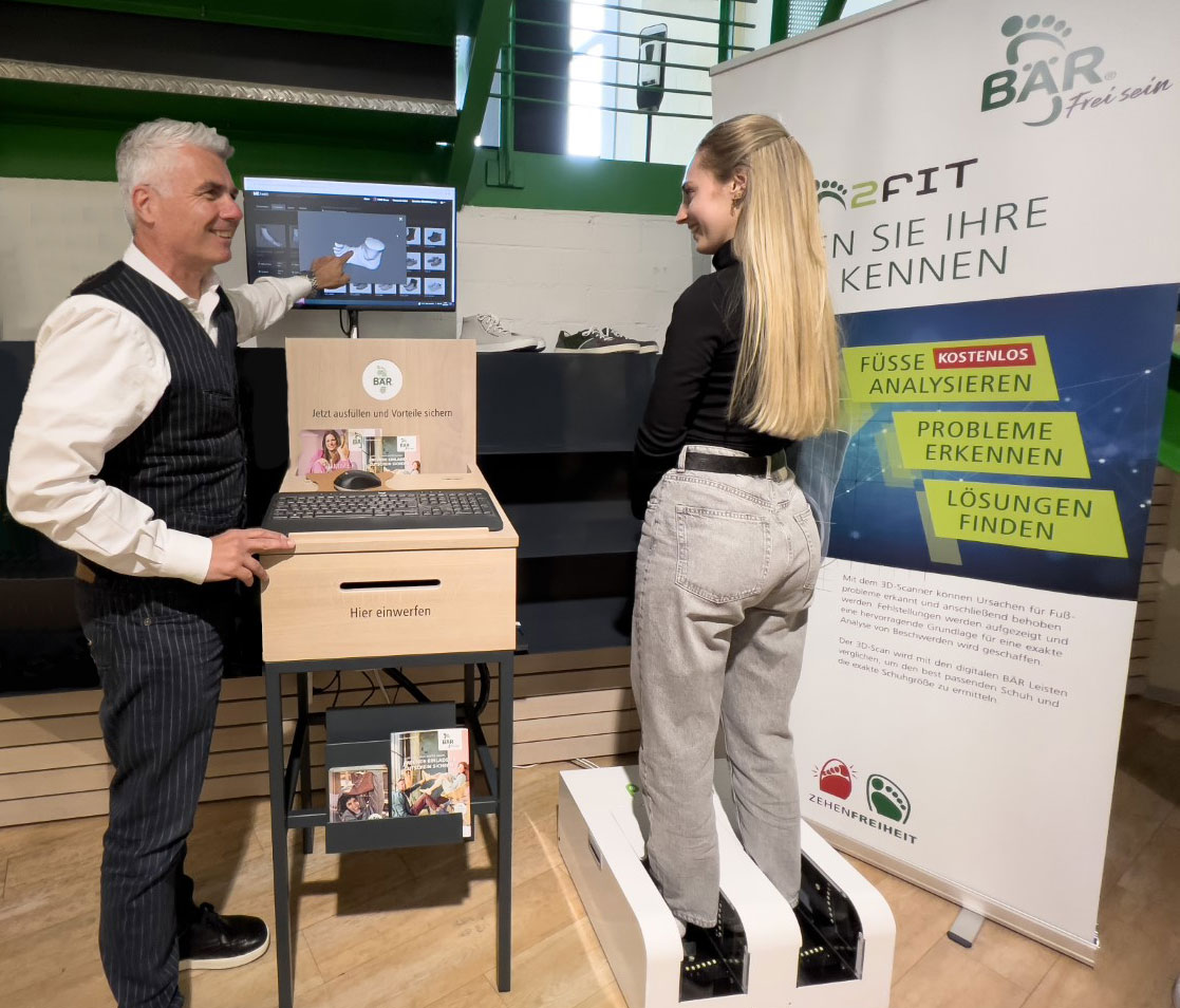Fußanalyse mit 3D-Scanner zur Erkennung von Problemen und Lösungen Ein Mann erklärt einer Frau die Fußanalyse mit einem 3D-Scanner an einem Stand der Marke BÄR.