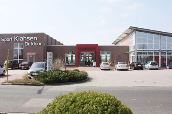 Eingangsbereich eines Sportgeschäfts mit großer Glasfassade und Parkplatz Außenansicht eines Sportgeschäfts mit Glasfront, Parkplatz und mehreren Autos