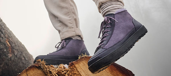 Stylish purple hiking boots on a tree stump A person wearing purple hiking boots standing on a cut tree stump, showcasing outdoor footwear
