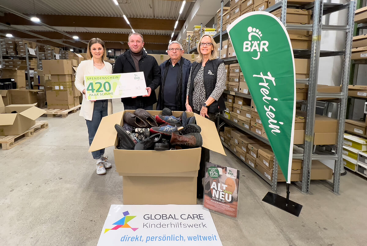 Spendenaktion von 420 Paar Schuhen an das Kinderhilfswerk GLOBAL CARE Gruppenfoto in einem Lager mit einer großen Schuhkarton-Spende an GLOBAL CARE
