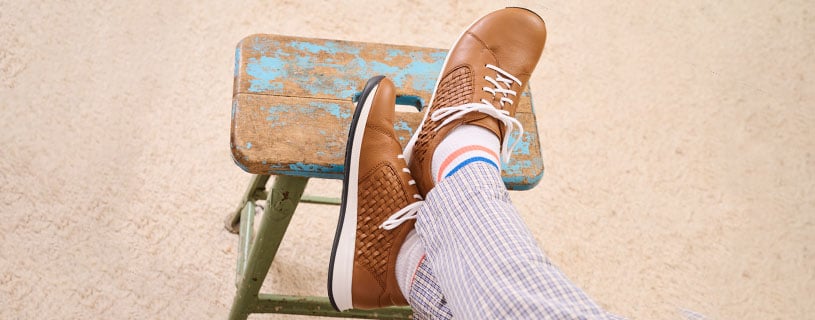 Braune Freizeitschuhe auf einem blauen Hocker Person trägt braune Freizeitschuhe und gestreifte Hose, Füße auf einem alten blauen Hocker