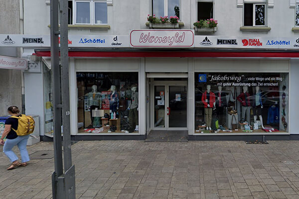 Außenansicht eines Outdoor- und Bekleidungsgeschäfts namens Wonsyld Eingangsbereich eines Outdoor- und Bekleidungsgeschäfts mit Schaufenster und Markenlogos wie Meindl und Schöffel. Eine Person mit gelbem Rucksack geht vorbei.
