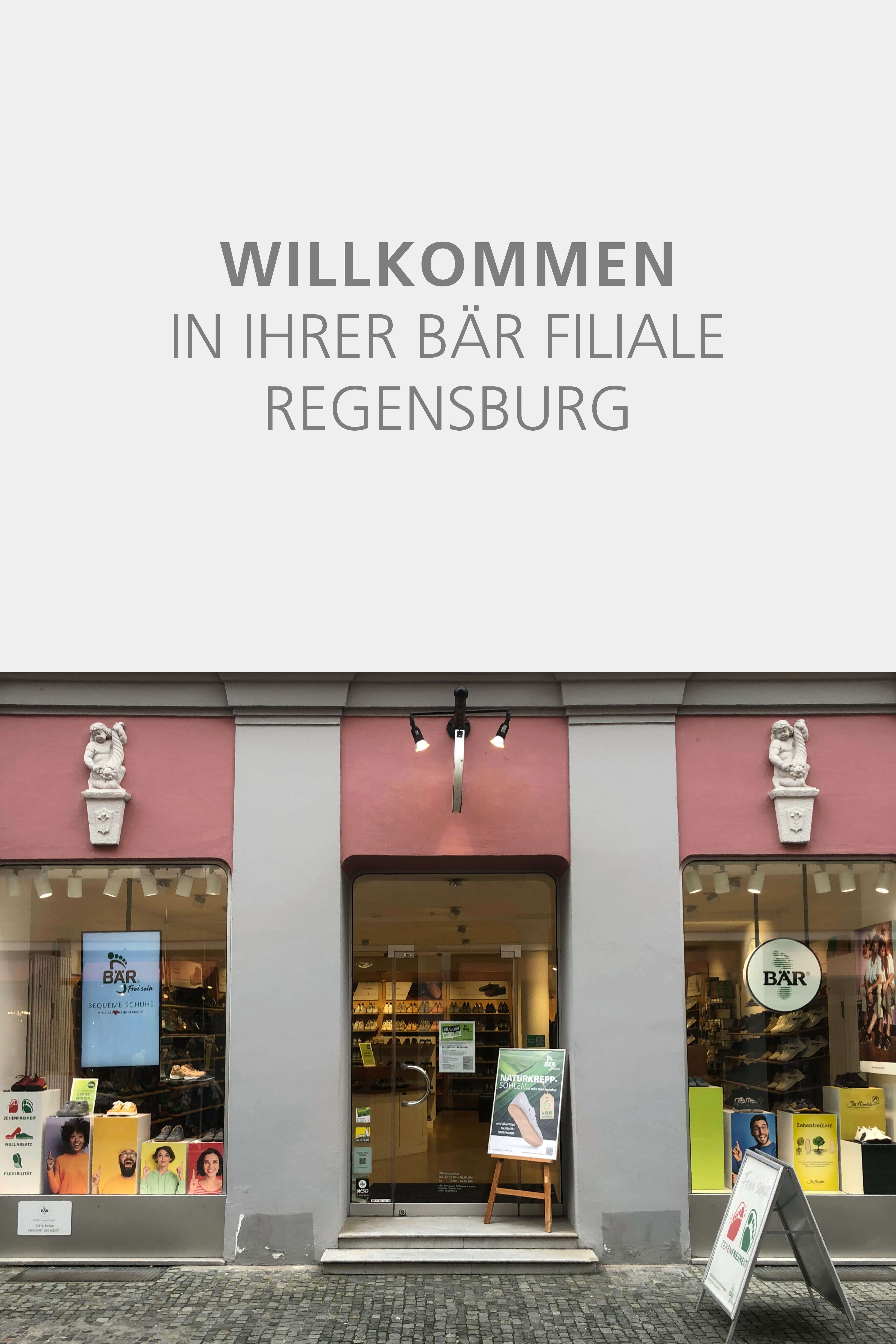 The front view of Bär shoe store in Regensburg, featuring a pink facade with two windows displaying shoes and a central glass door with welcome signage above.