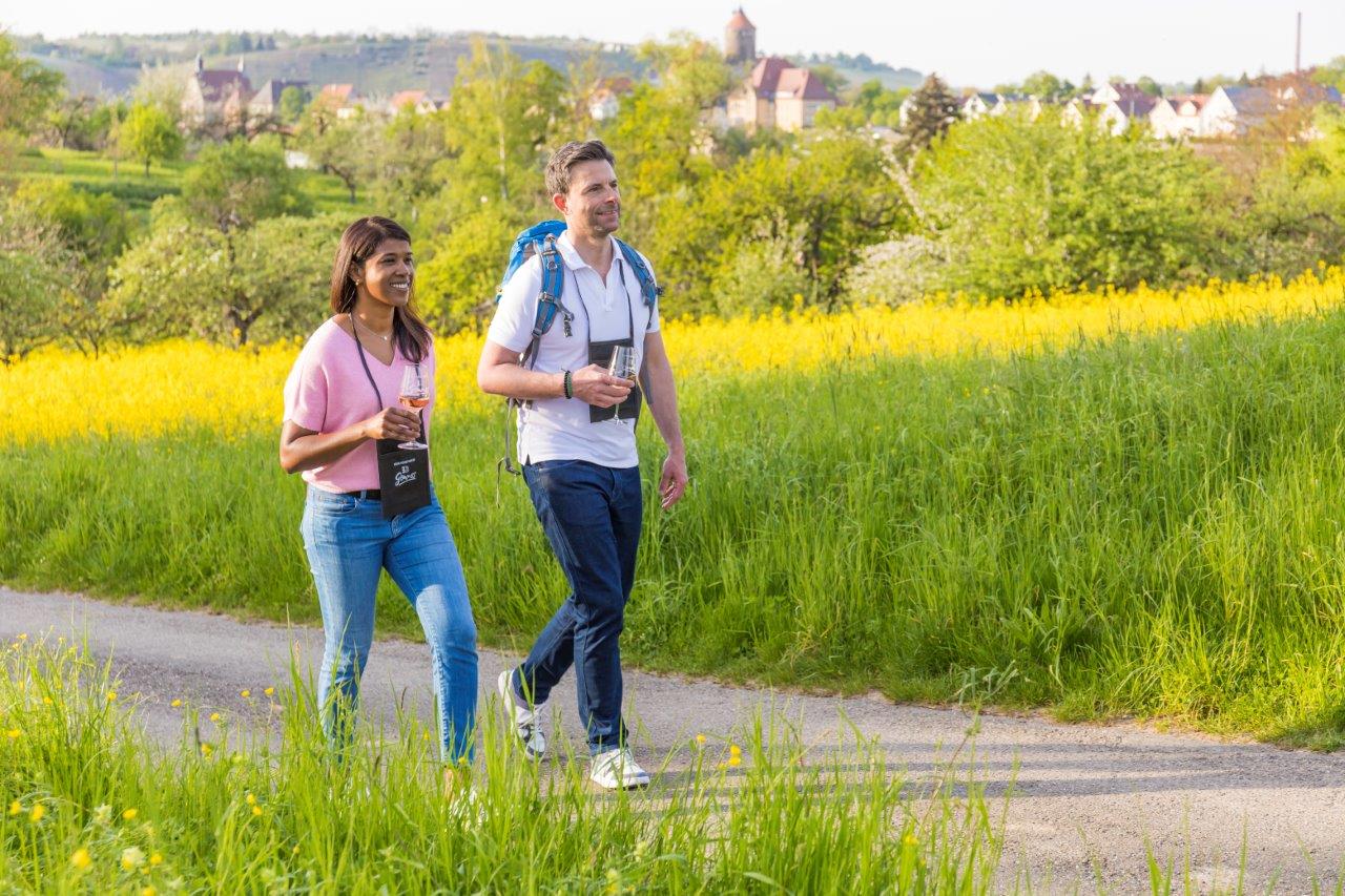 Couple enjoying a wine walk in the countryside A couple walking through a green field holding wine glasses, with a scenic village view in the background