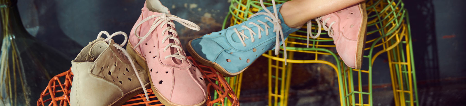 Stylish perforated leather sneakers in pink, blue, and beige on modern chairs Close-up of perforated leather sneakers in pink, blue, and beige displayed on colorful wire chairs