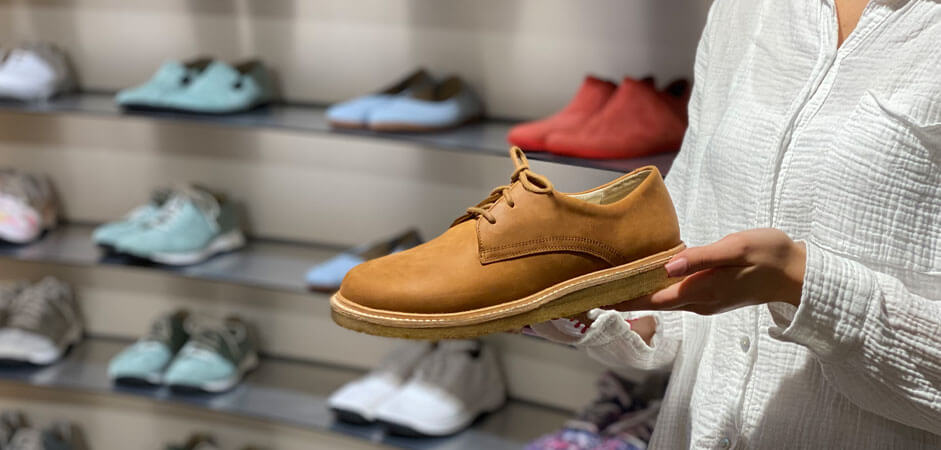 Elegant leather shoe showcased in a store Person holding a brown leather shoe in a shop with various shoes displayed on shelves