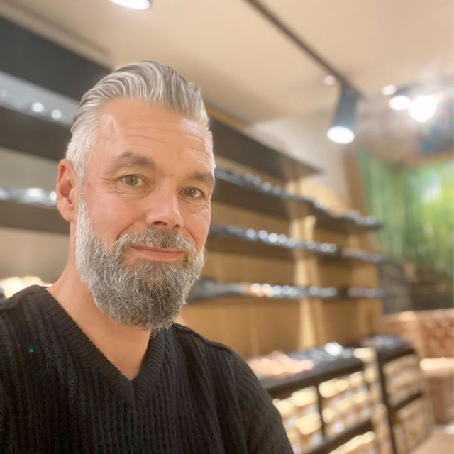 Mann vor Regal in einem Geschäft Ein Mann mit grauem Haar und Bart steht vor einem Regal in einem Geschäft und lächelt in die Kamera.