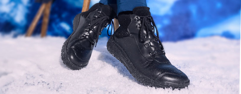 Nahaufnahme von wasserdichten schwarzen Winterstiefeln auf schneebedecktem Boden