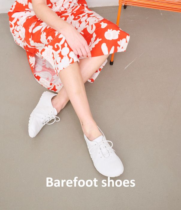 A woman in a red and white floral dress wearing white barefoot shoes, seated on an orange chair