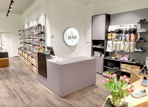 Moderner Schuh- und Accessoire-Laden mit heller Einrichtung Innenansicht eines modernen Schuhladens mit Regalen voller Schuhe und Accessoires, einem grauen Tresen und einem Blumenstrauß auf einem Tisch