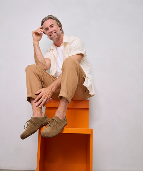 Man in casual beige clothing sitting on an orange chair, smiling