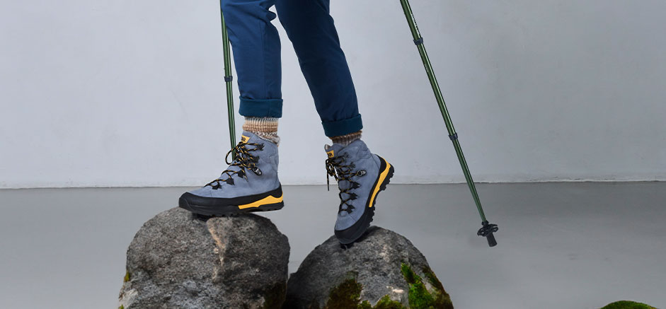 Person wearing sturdy hiking boots climbing rocks, using trekking poles for support.