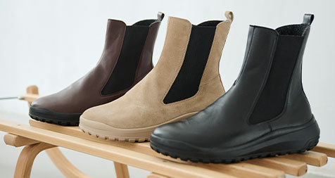 Stylish Chelsea Boots in Brown, Beige, and Black on Wooden Rack Three pairs of Chelsea boots in brown, beige, and black displayed on a wooden rack.