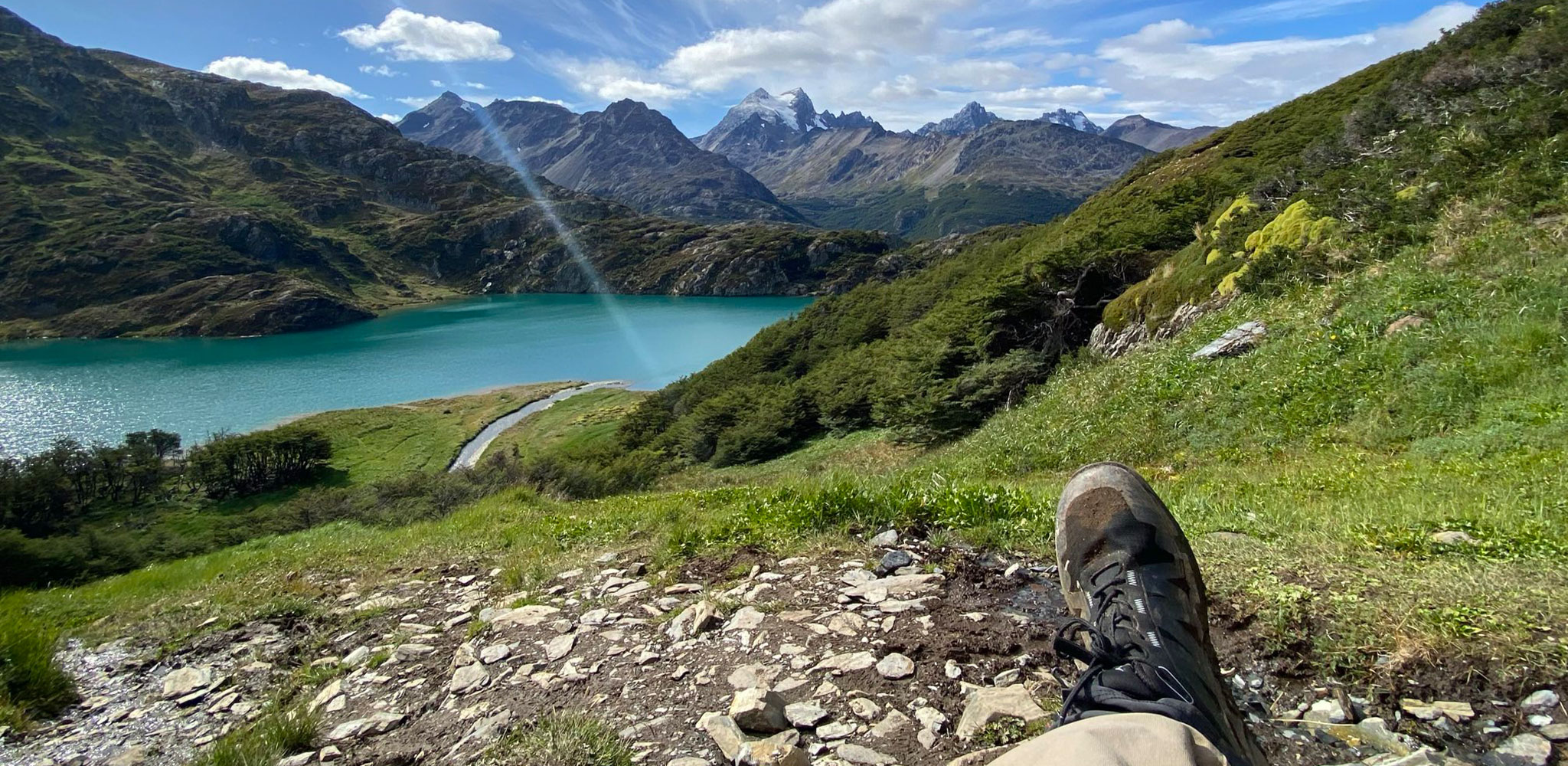 Relaxing with a Scenic Mountain and Lake View Person resting on a hillside overlooking a turquoise lake and mountain range on a sunny day.