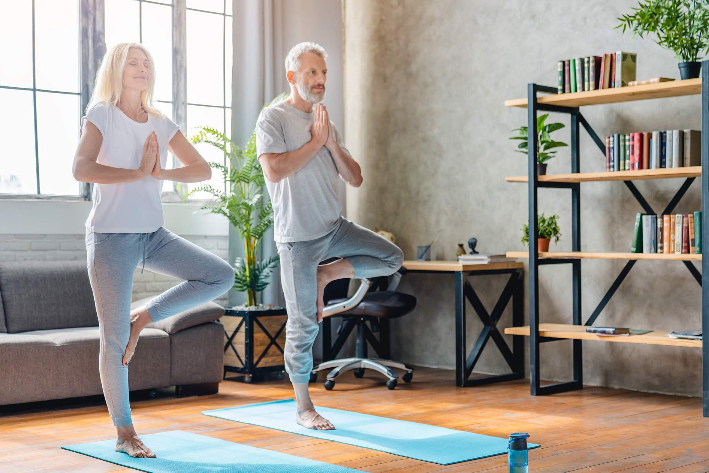 Couple practicing yoga in a bright cozy living room Man and woman performing tree pose yoga exercise on mats at home
