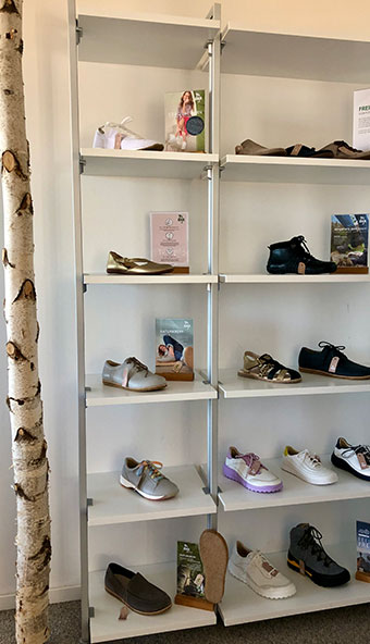 Moderne Schuhpräsentation in einem Regal Ein weißes Regal zeigt eine Auswahl verschiedener Schuhe, darunter Sneaker und Sandalen, in einem Laden. Ein Birkenstamm steht daneben.